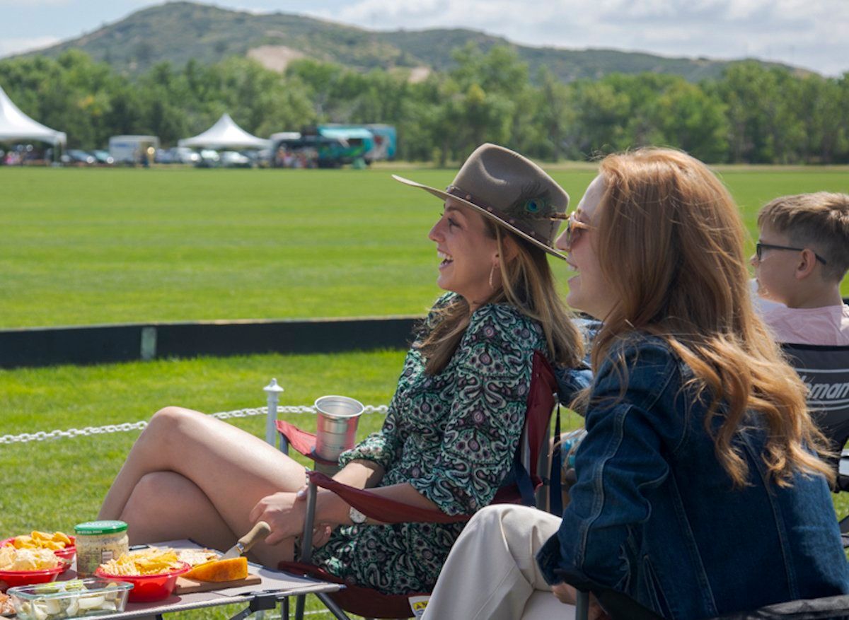Two women are sitting in chairs on a field talking to each other.