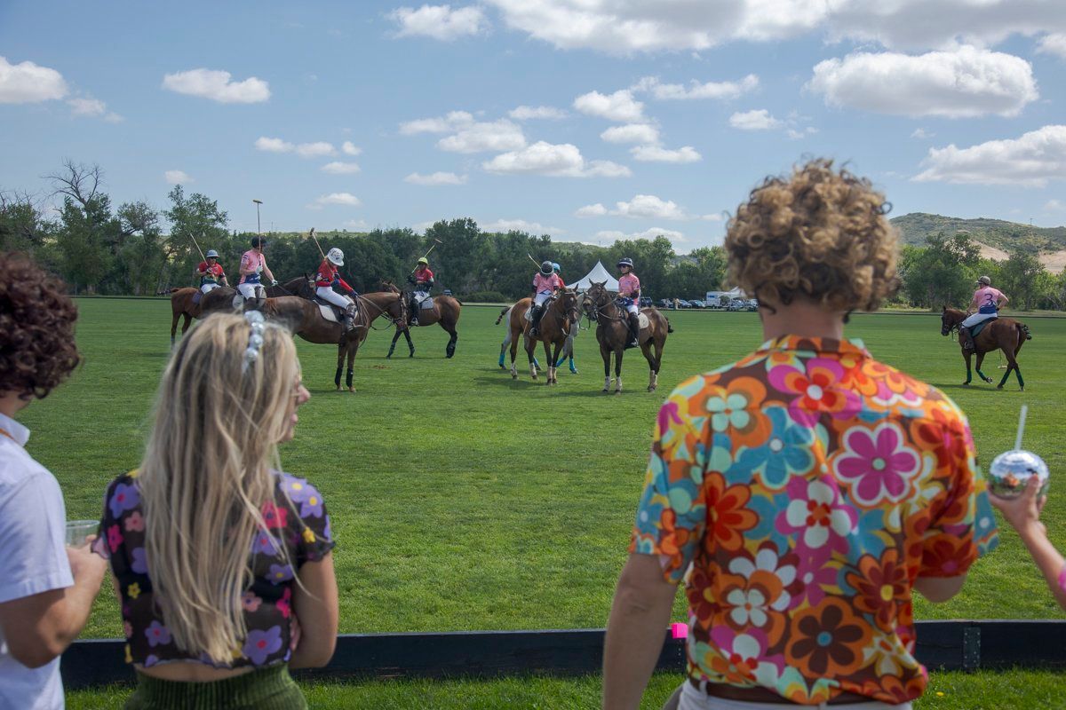 A group of people are watching a polo match on a field.