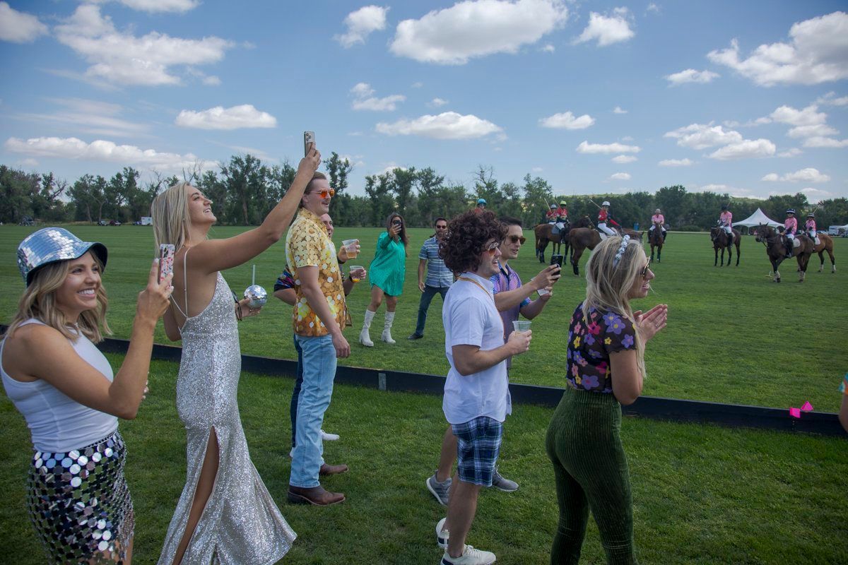 A group of people are standing in a field watching a polo match.
