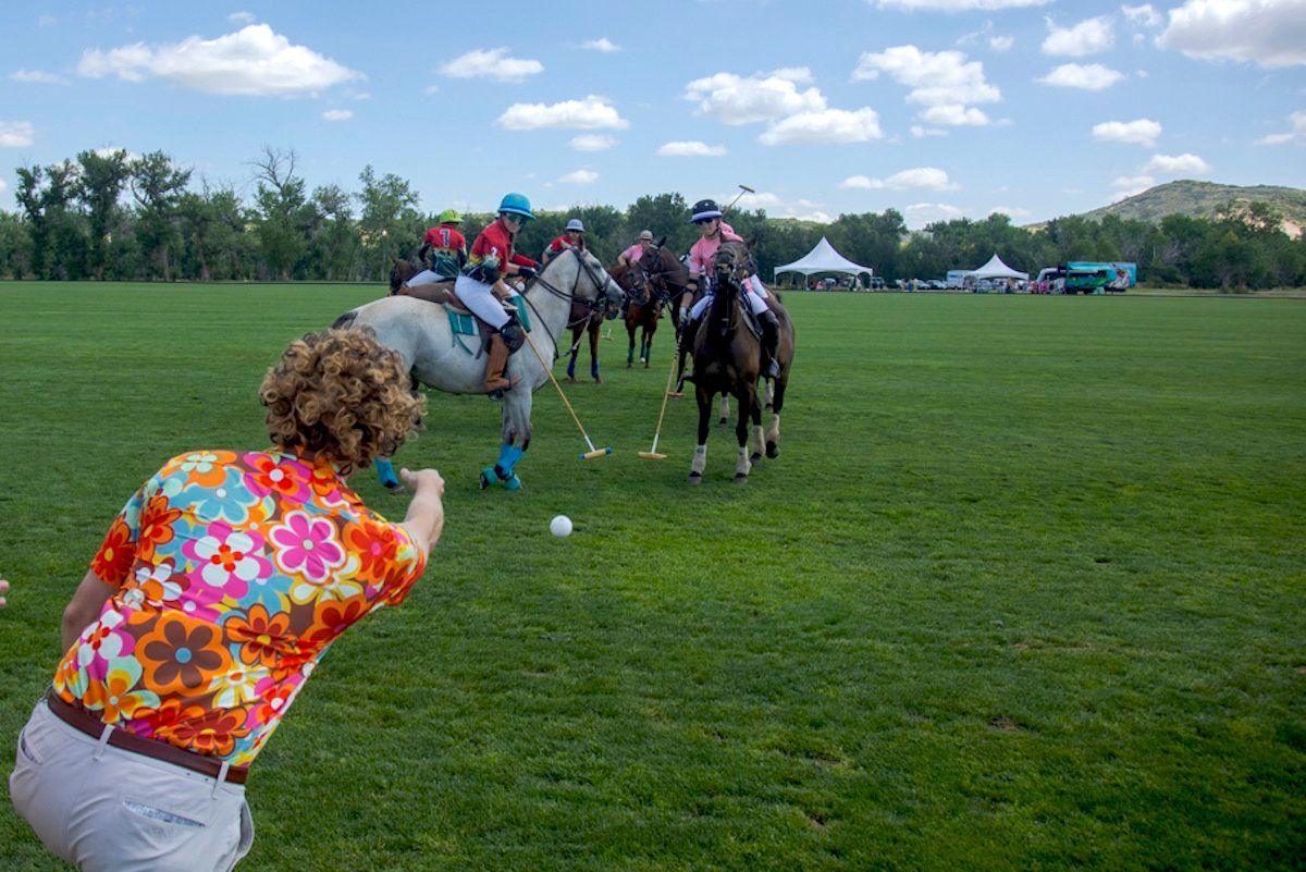 A woman is taking a picture of a polo game being played on a field.