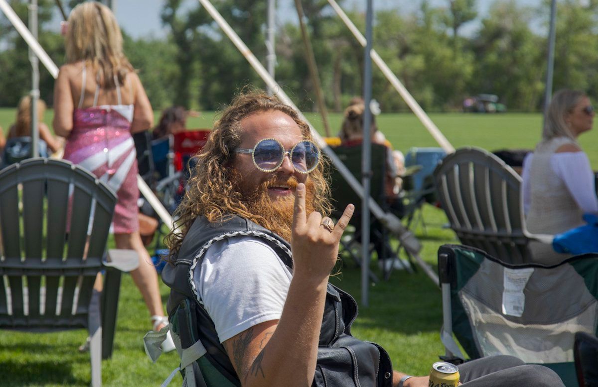 A man with a beard and sunglasses is sitting in a chair in a park.