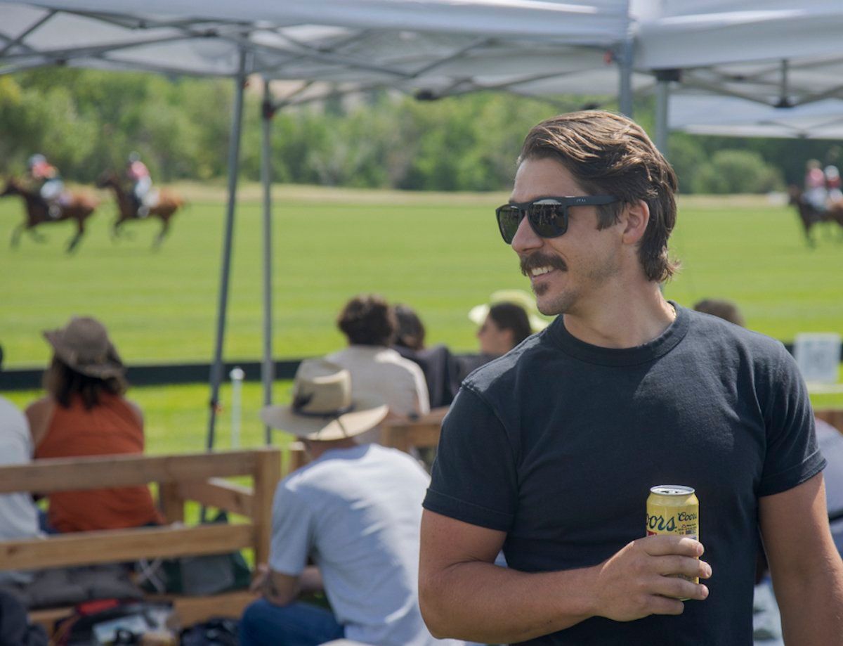 A man wearing sunglasses is holding a can of beer.