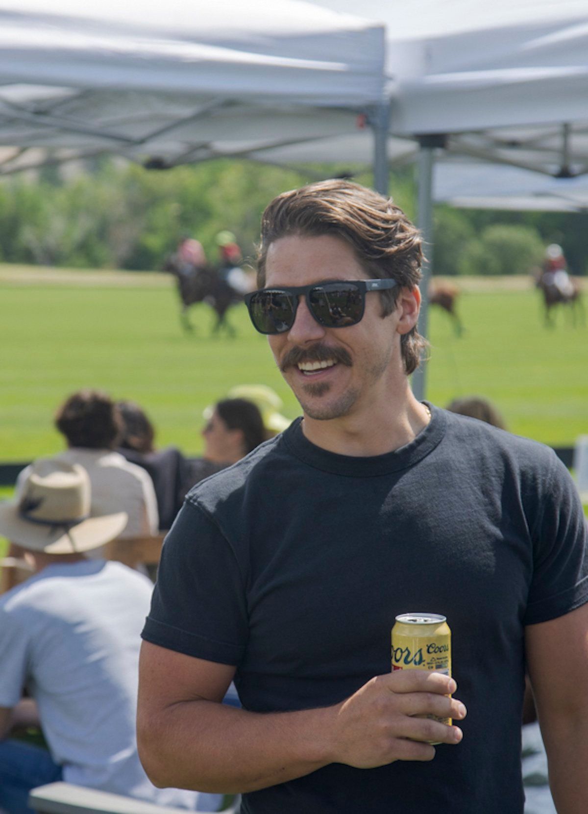 A man wearing sunglasses and a mustache is holding a can of soda.