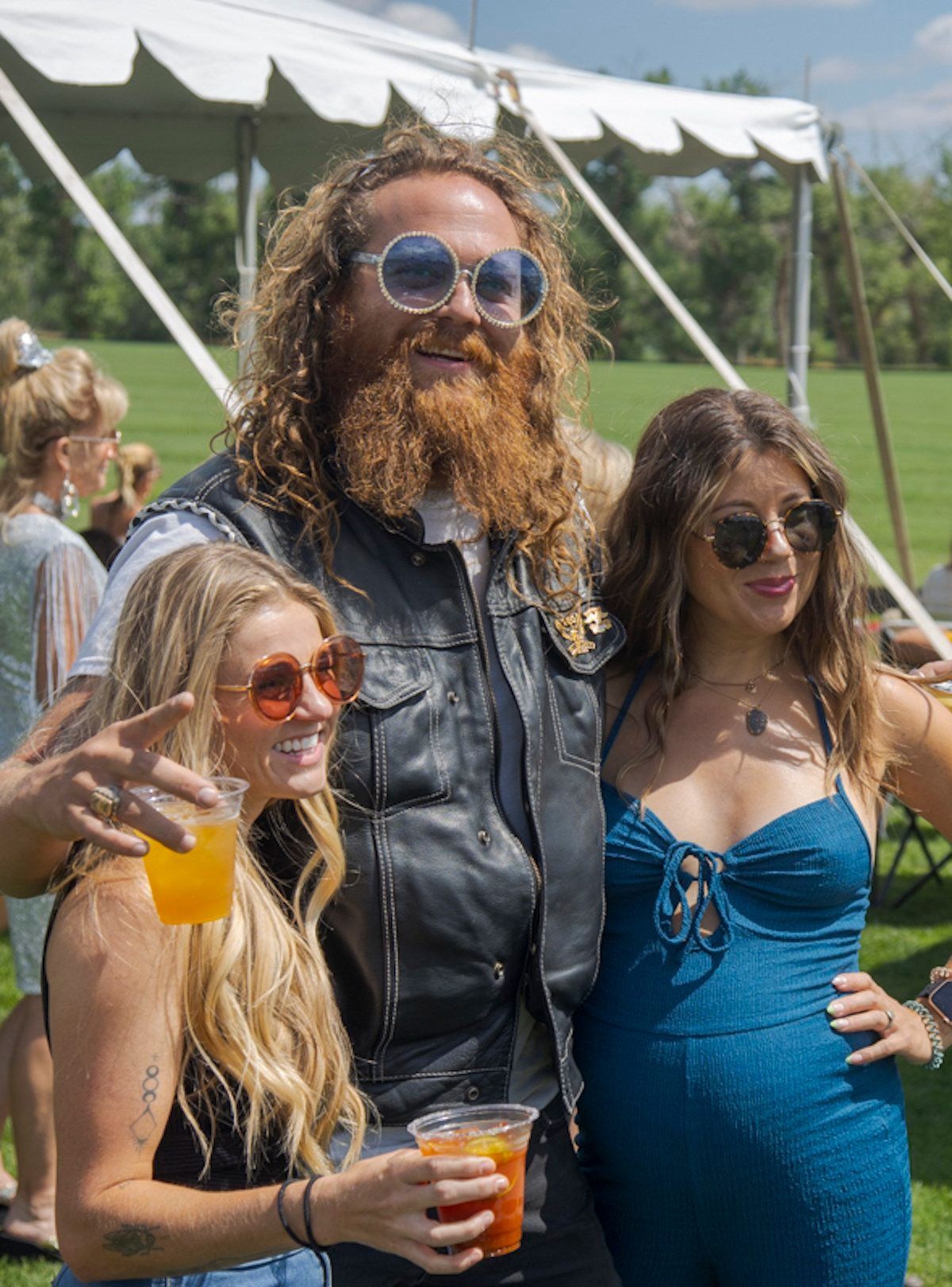 A man with a beard is standing next to two women holding drinks.
