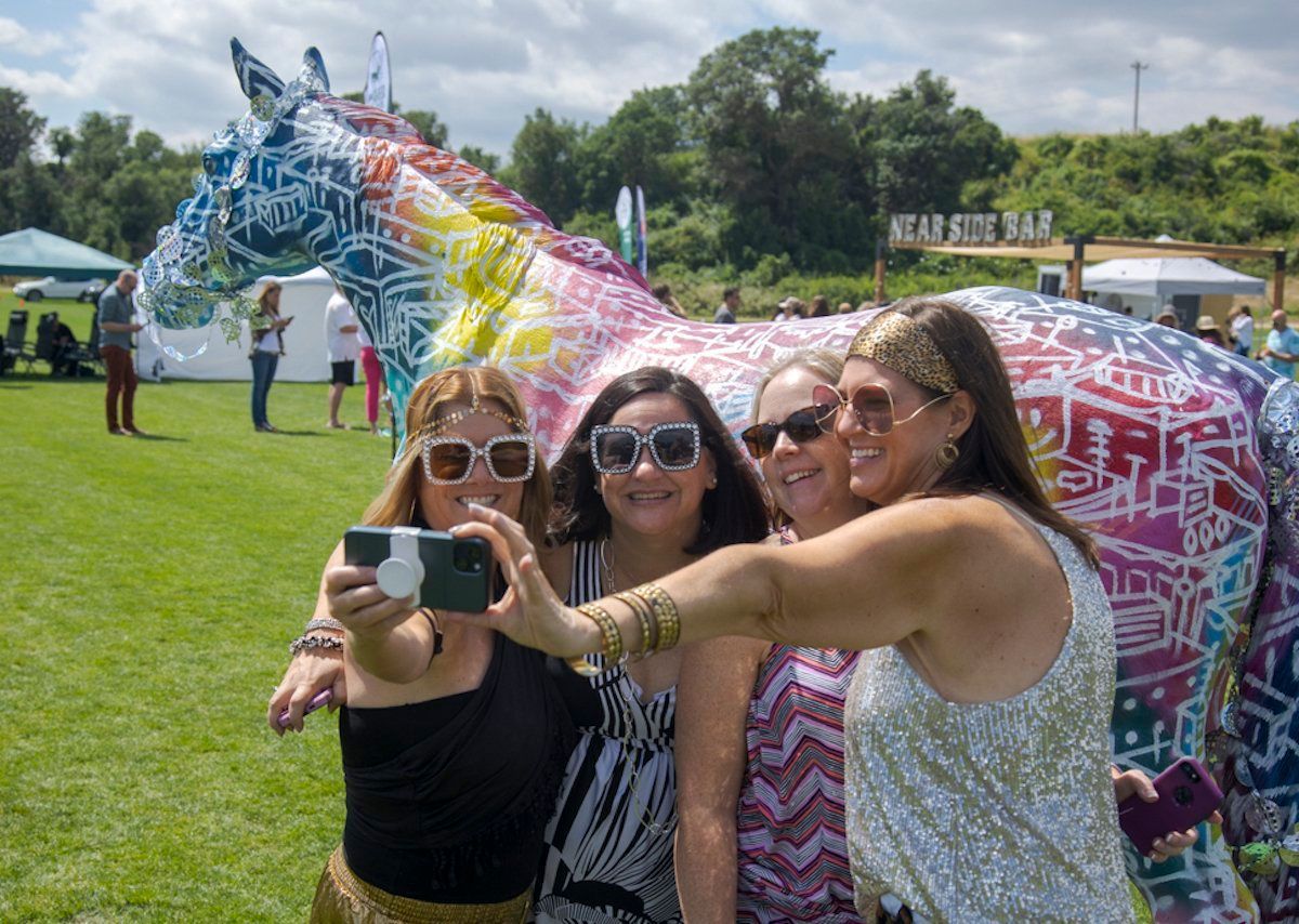 A group of women are taking a selfie in front of a colorful statue of a horse.