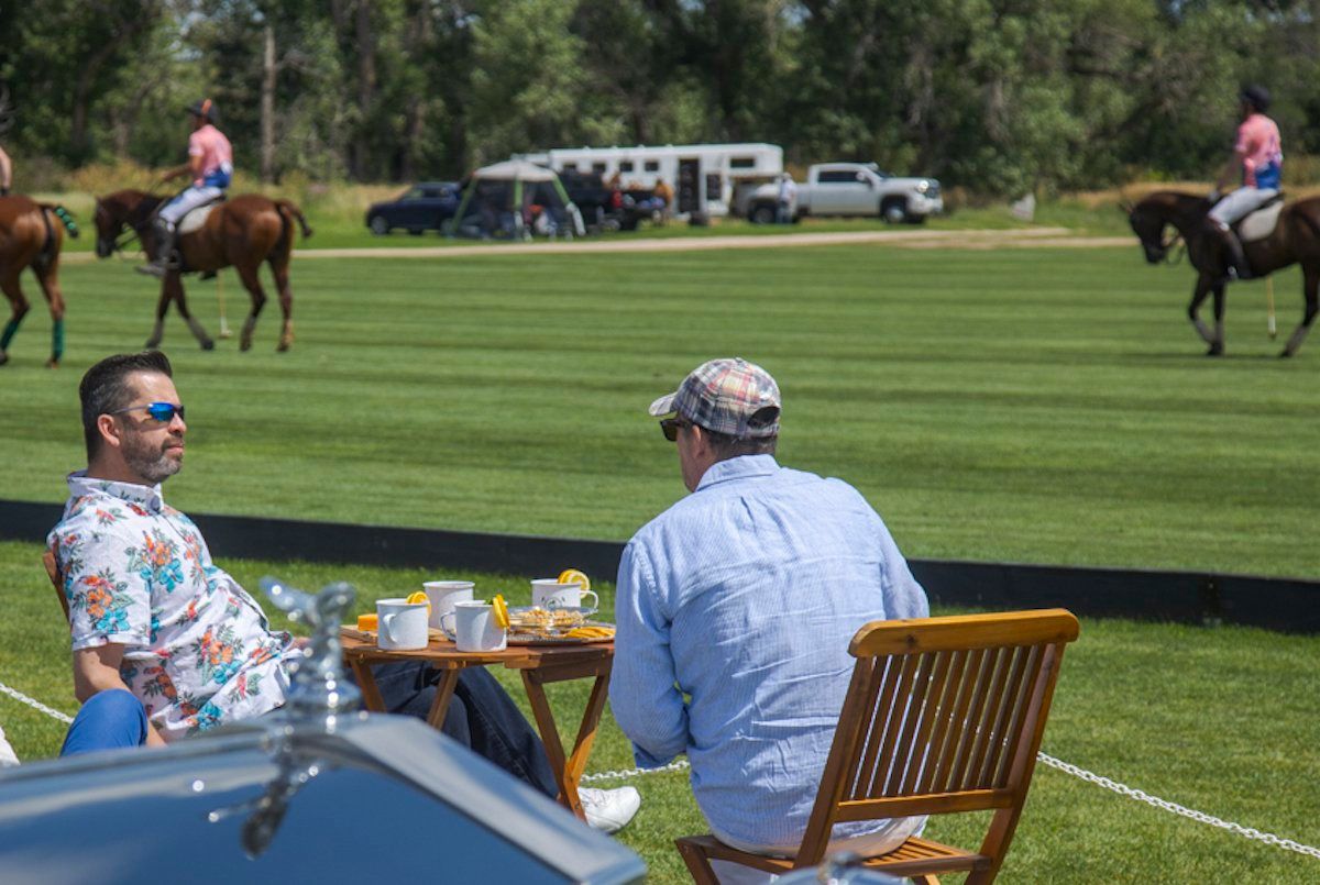 Two men are sitting at a table watching a polo match.