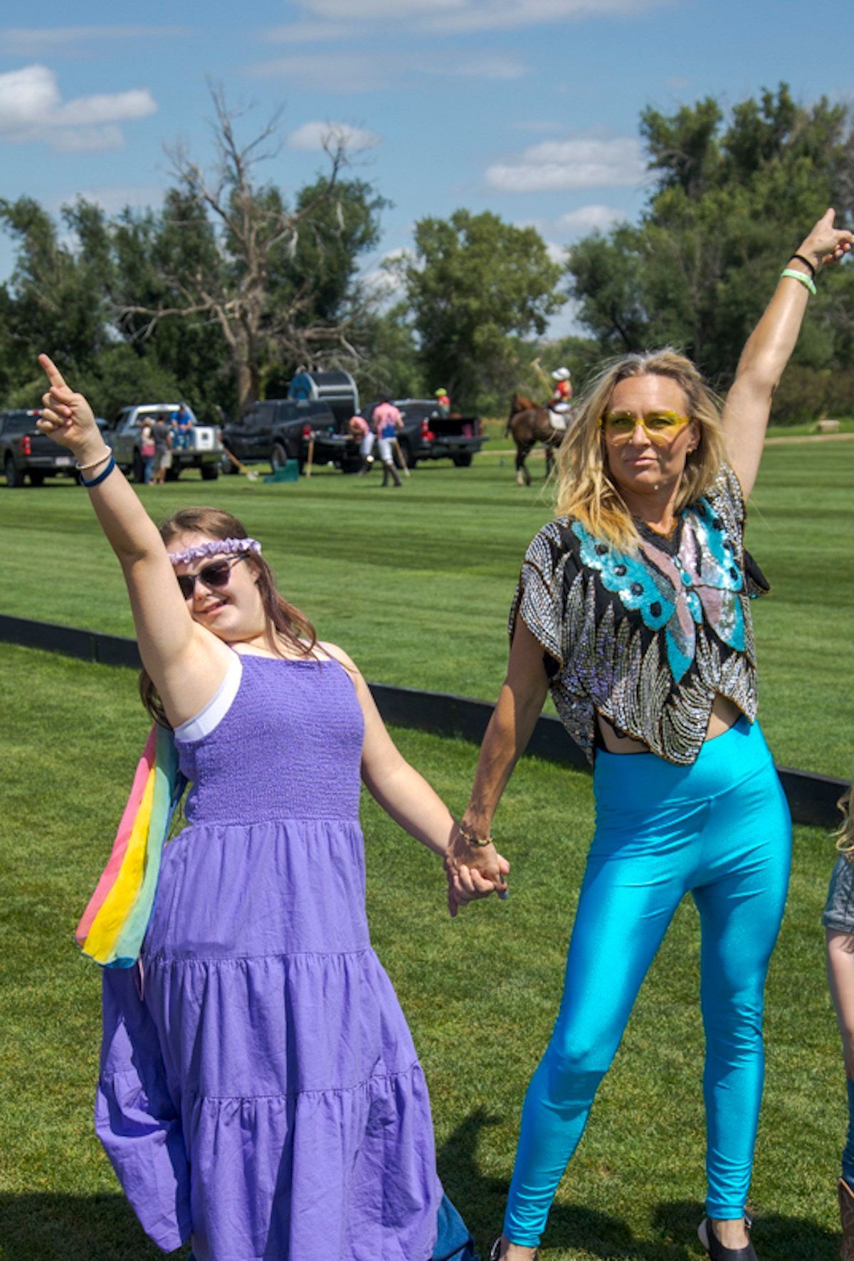 A woman in a purple dress and a woman in blue pants are holding hands in a field.