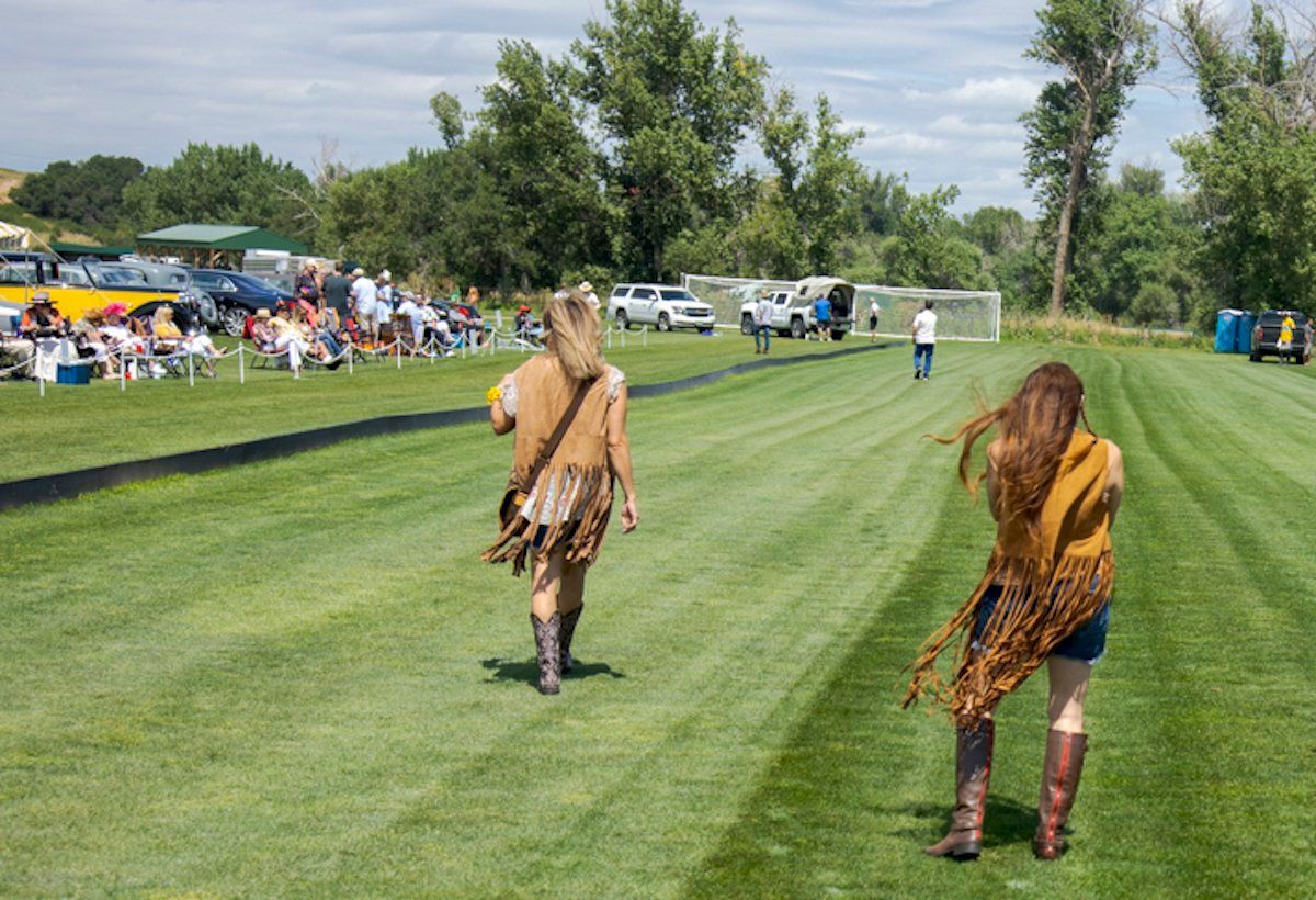 Two women are walking across a lush green field.