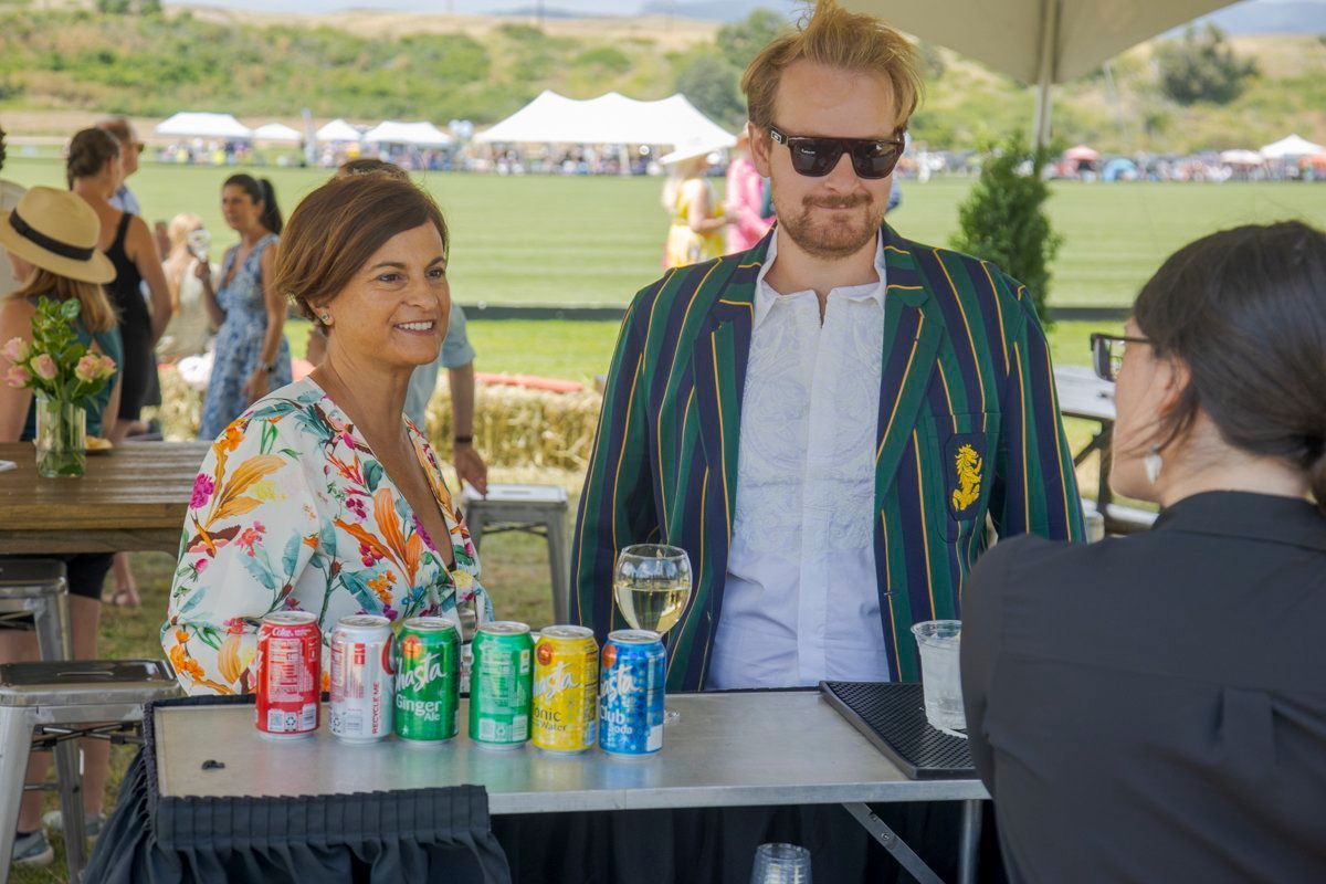 A man and a woman are standing next to each other at a table with cans of soda on it.