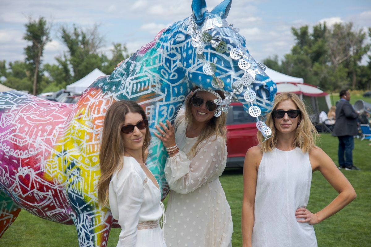 Three women are posing for a picture in front of a colorful horse statue.