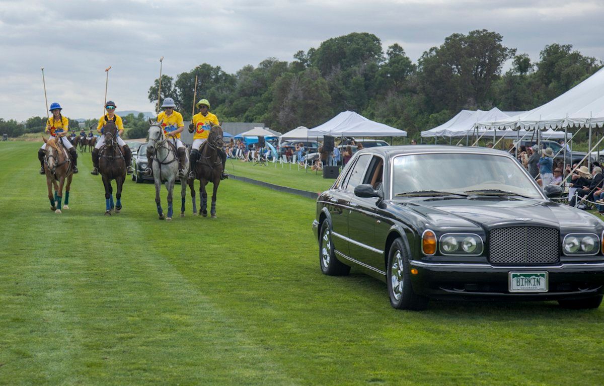 A group of people riding horses in a field with a limousine in the foreground.