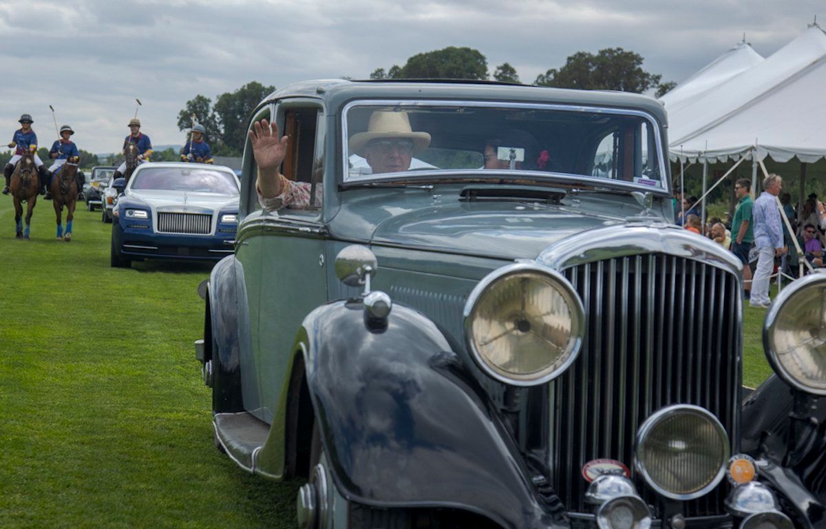 A man is waving from the window of an old car.