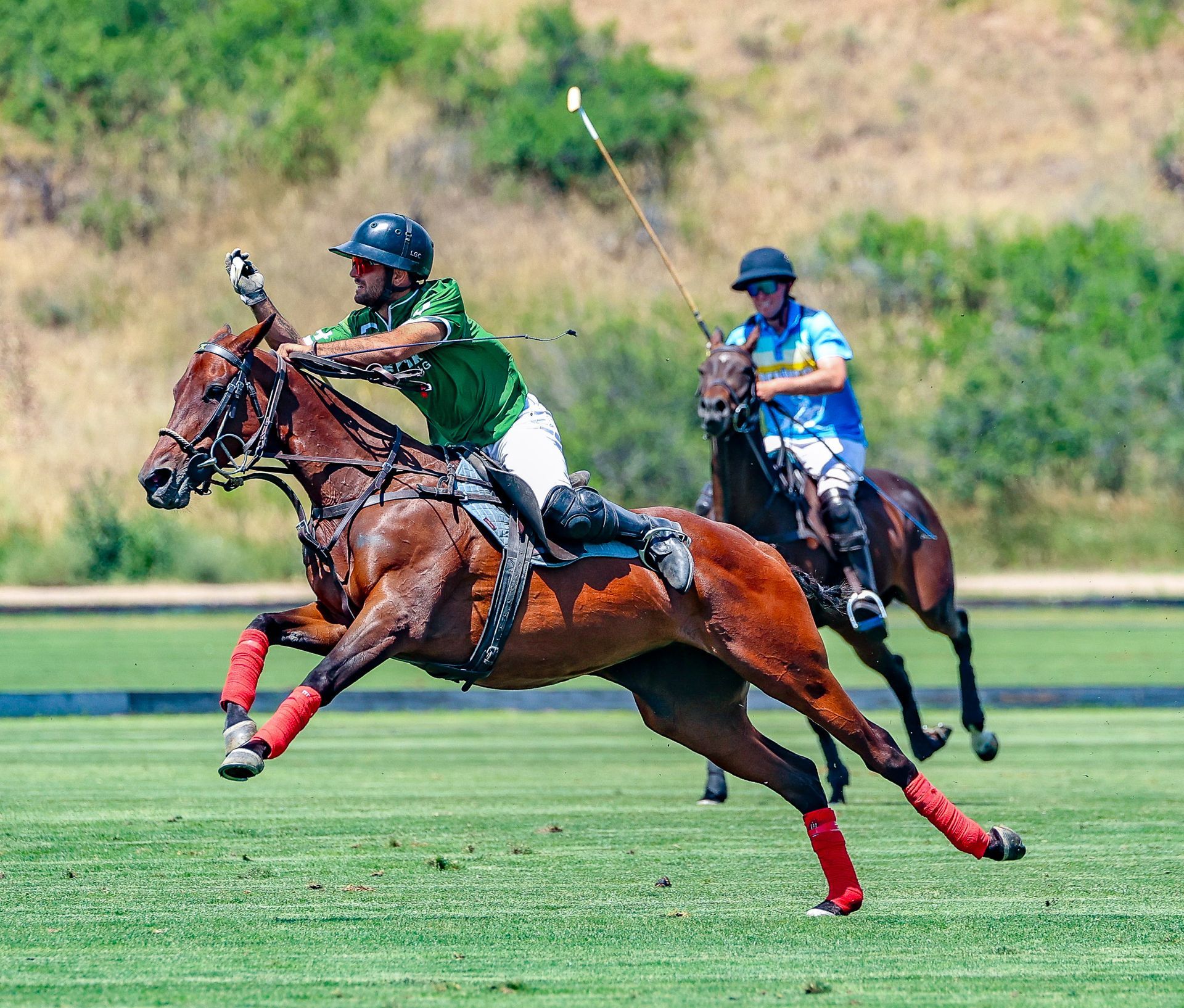 Polo match: Player in green swings mallet from horseback; another player follows behind on field.