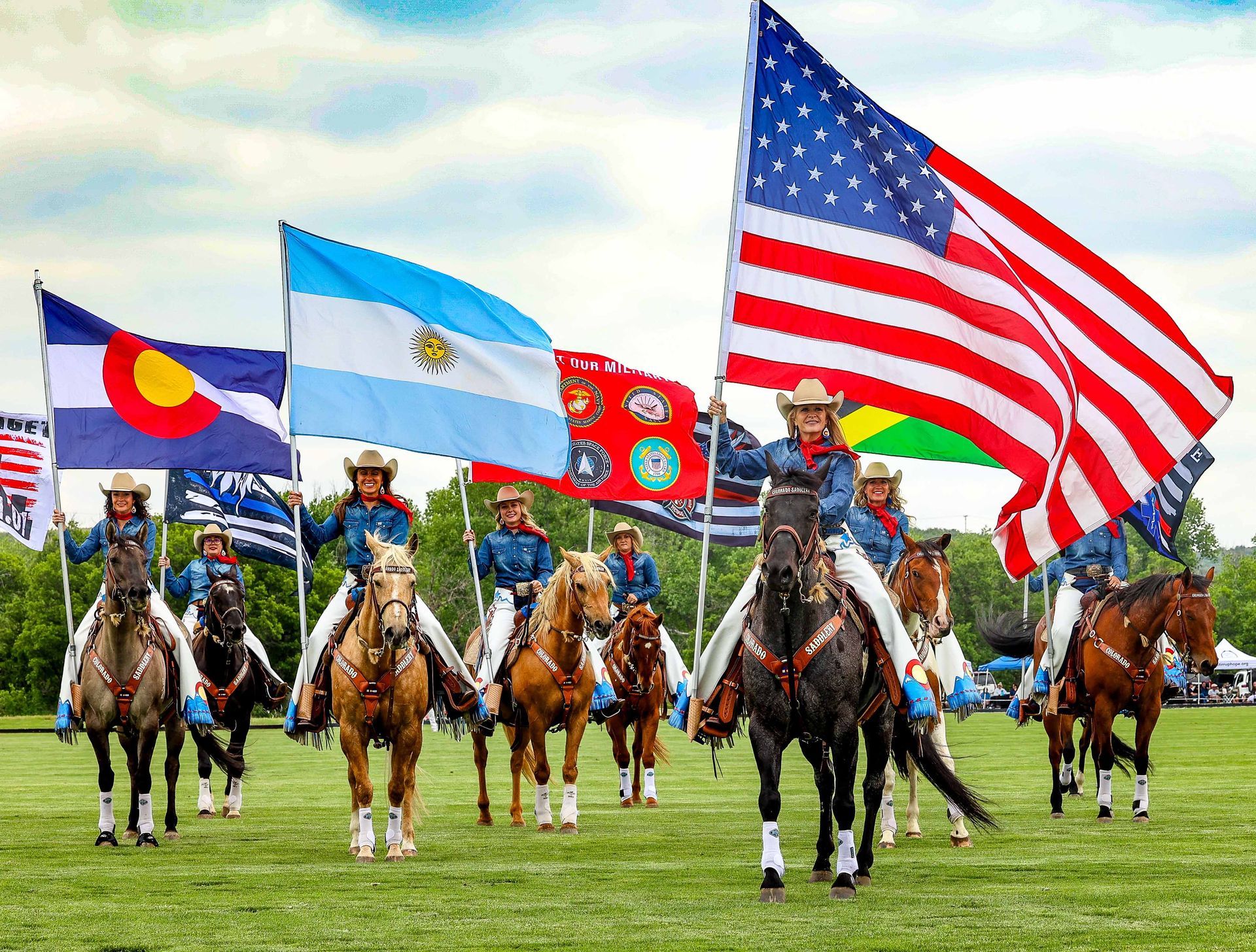Cowboy riders on horseback hold flags including the American flag, Colorado flag, and Argentina flag.