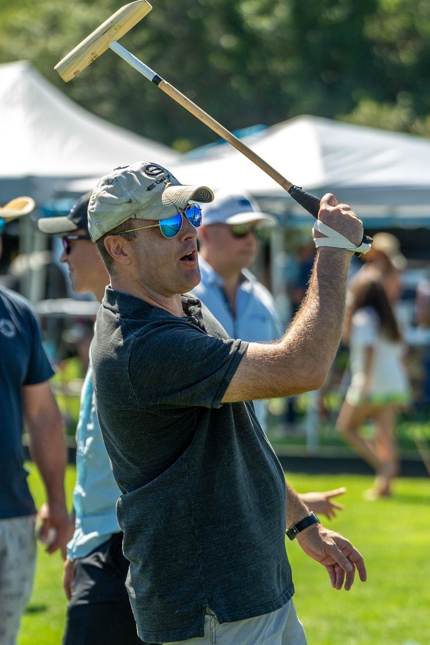 A man wearing sunglasses and a hat is throwing a stick in the air.