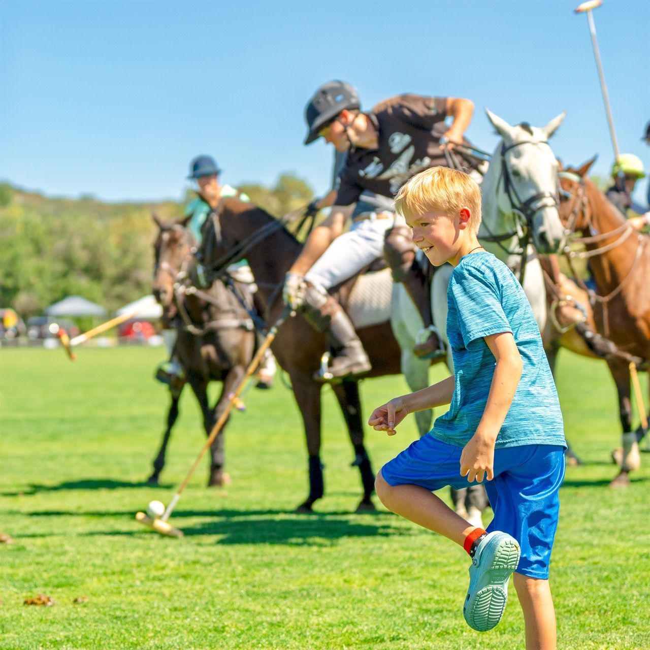 A young boy is kicking a ball while riding a horse.