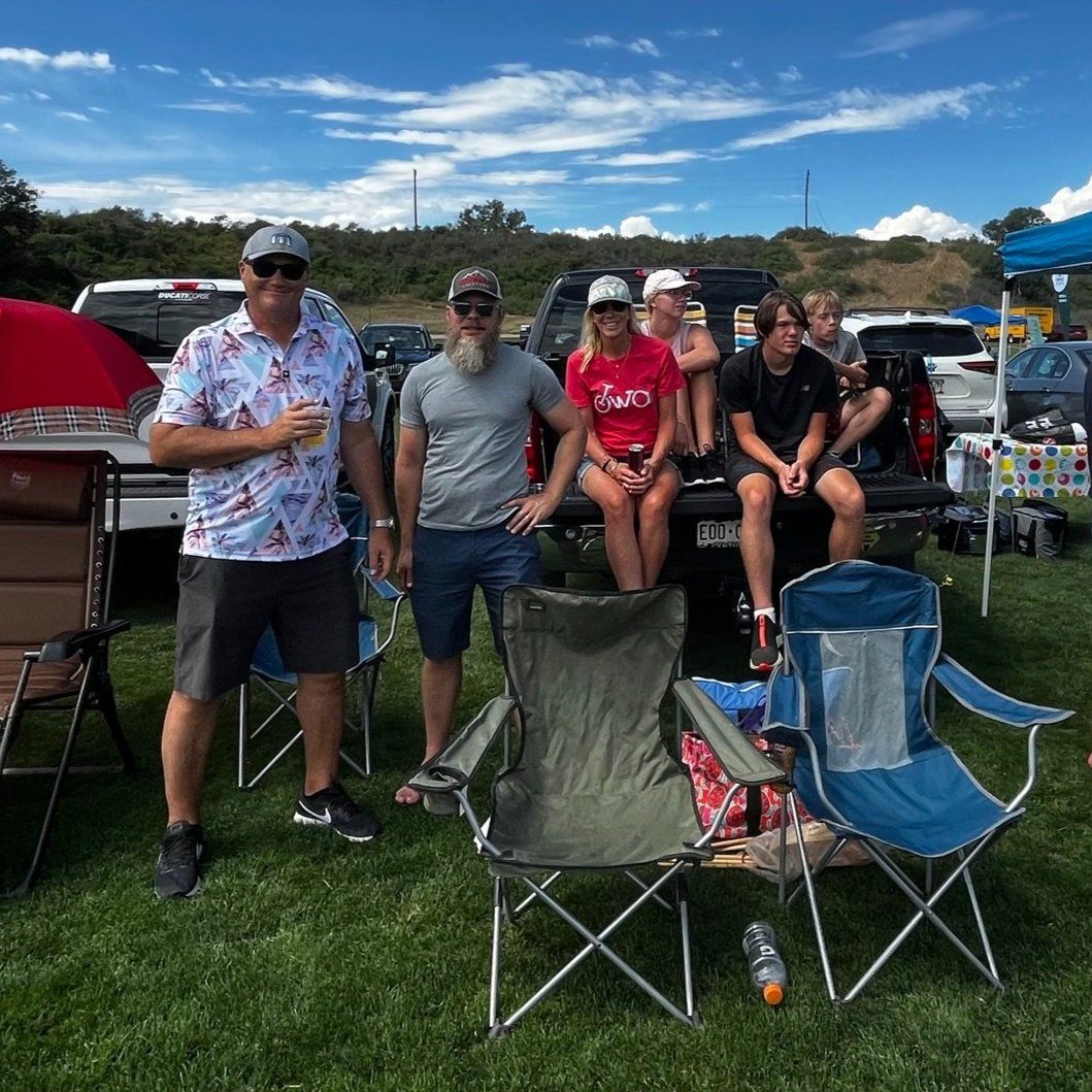 A group of people standing next to folding chairs in a field.