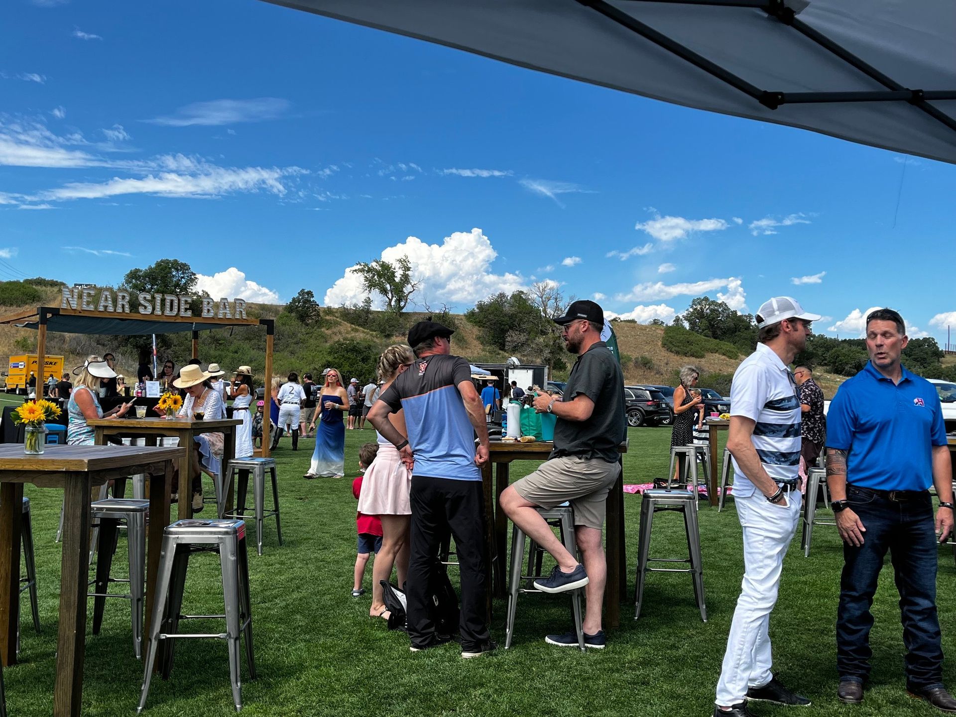 A group of people are standing around tables in a field.