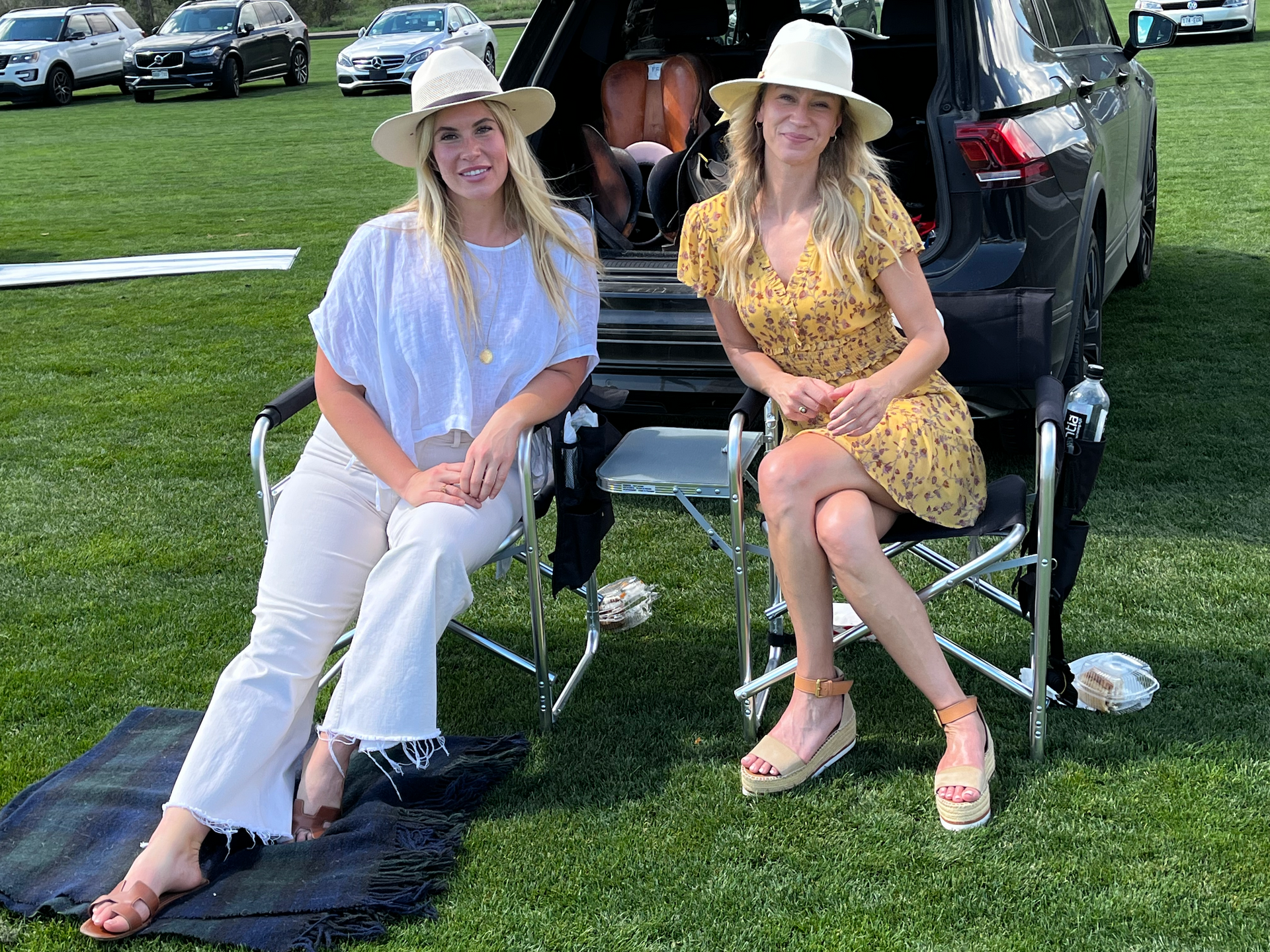 Two women are sitting in folding chairs in front of a car.