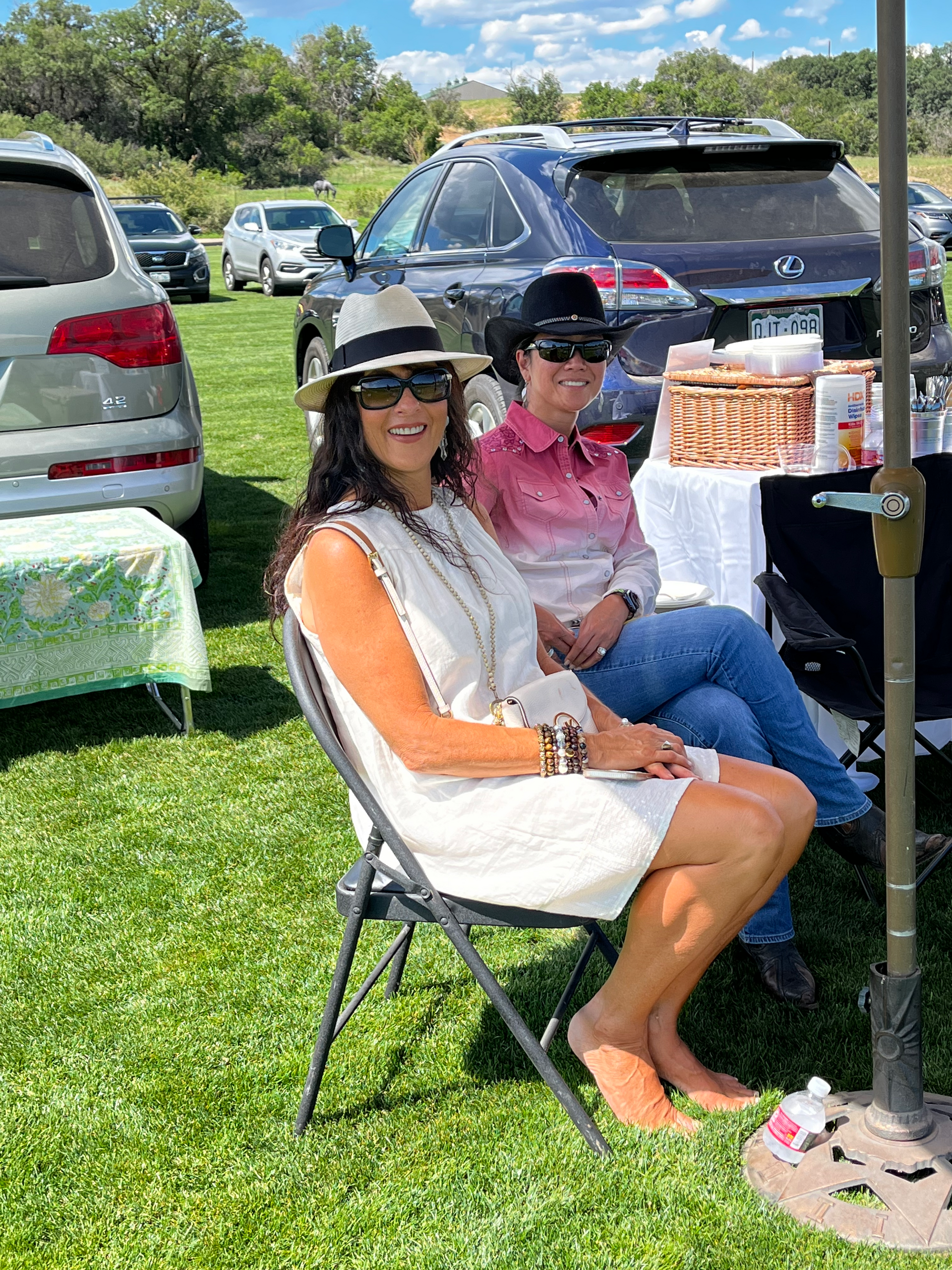 Two women are sitting in folding chairs in a grassy field.