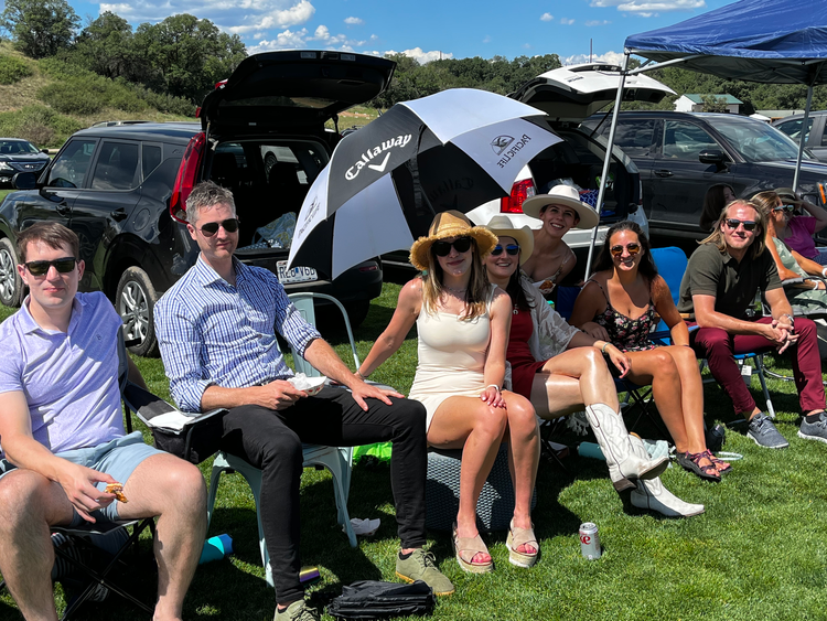 A group of people are sitting in the grass under an umbrella.