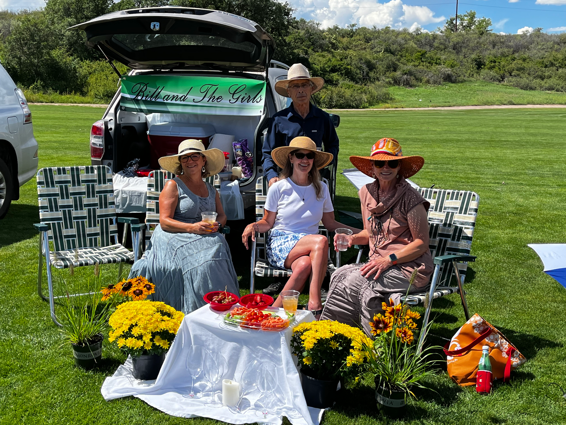 A group of people are sitting in chairs in front of a car trunk.