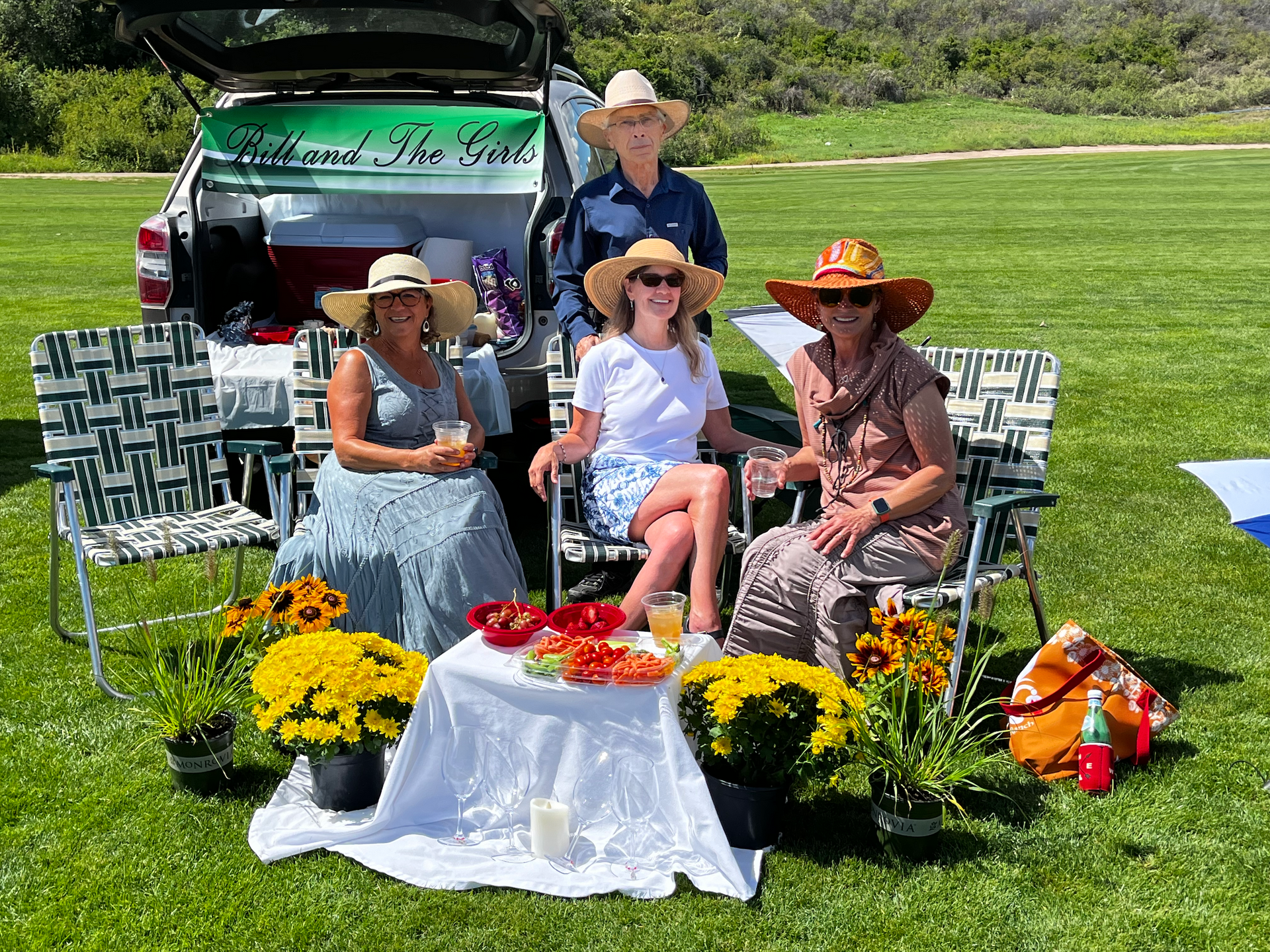 A group of people are sitting in the grass in front of a car.