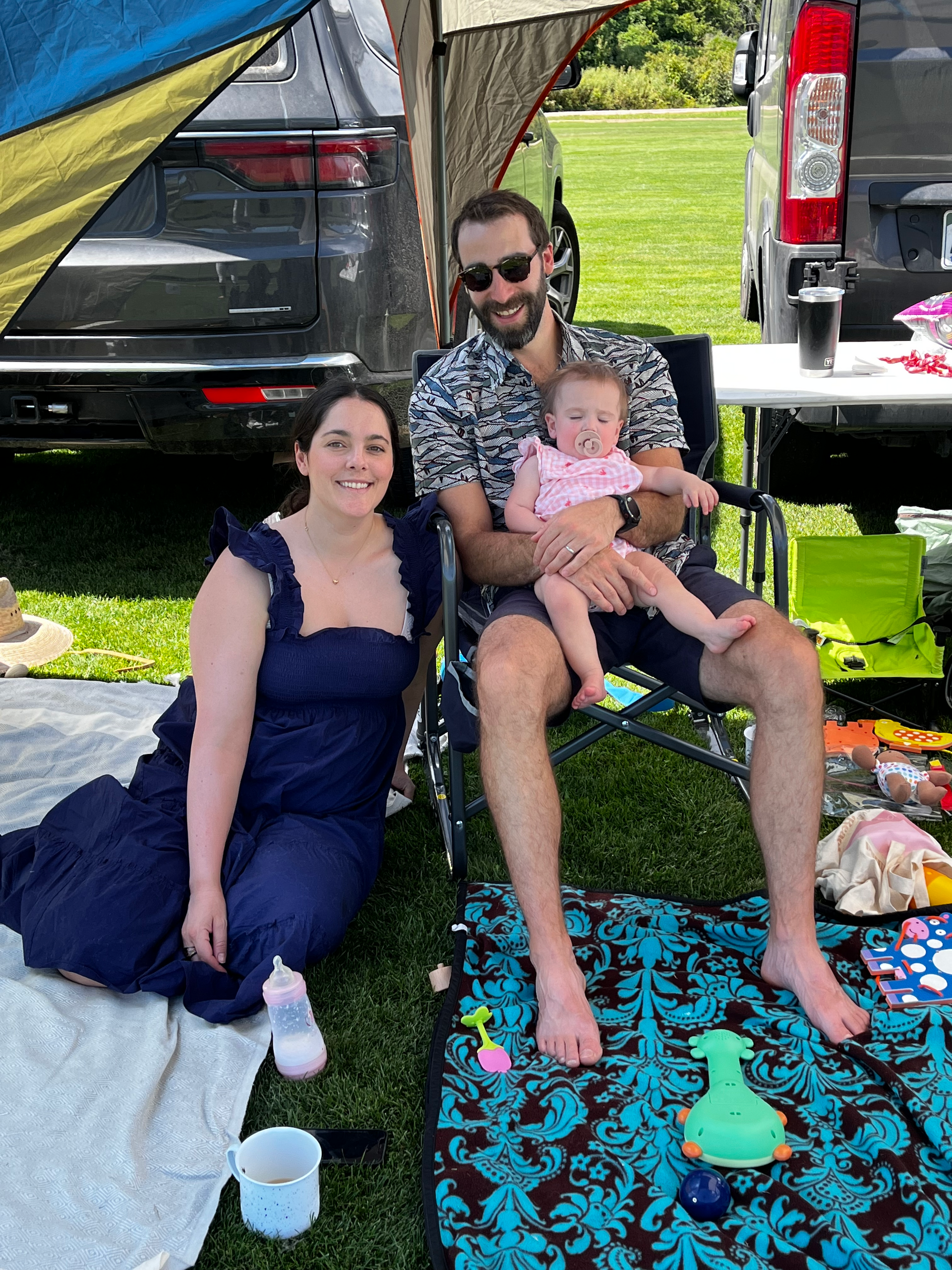 A man and a woman are sitting on a blanket with a baby.