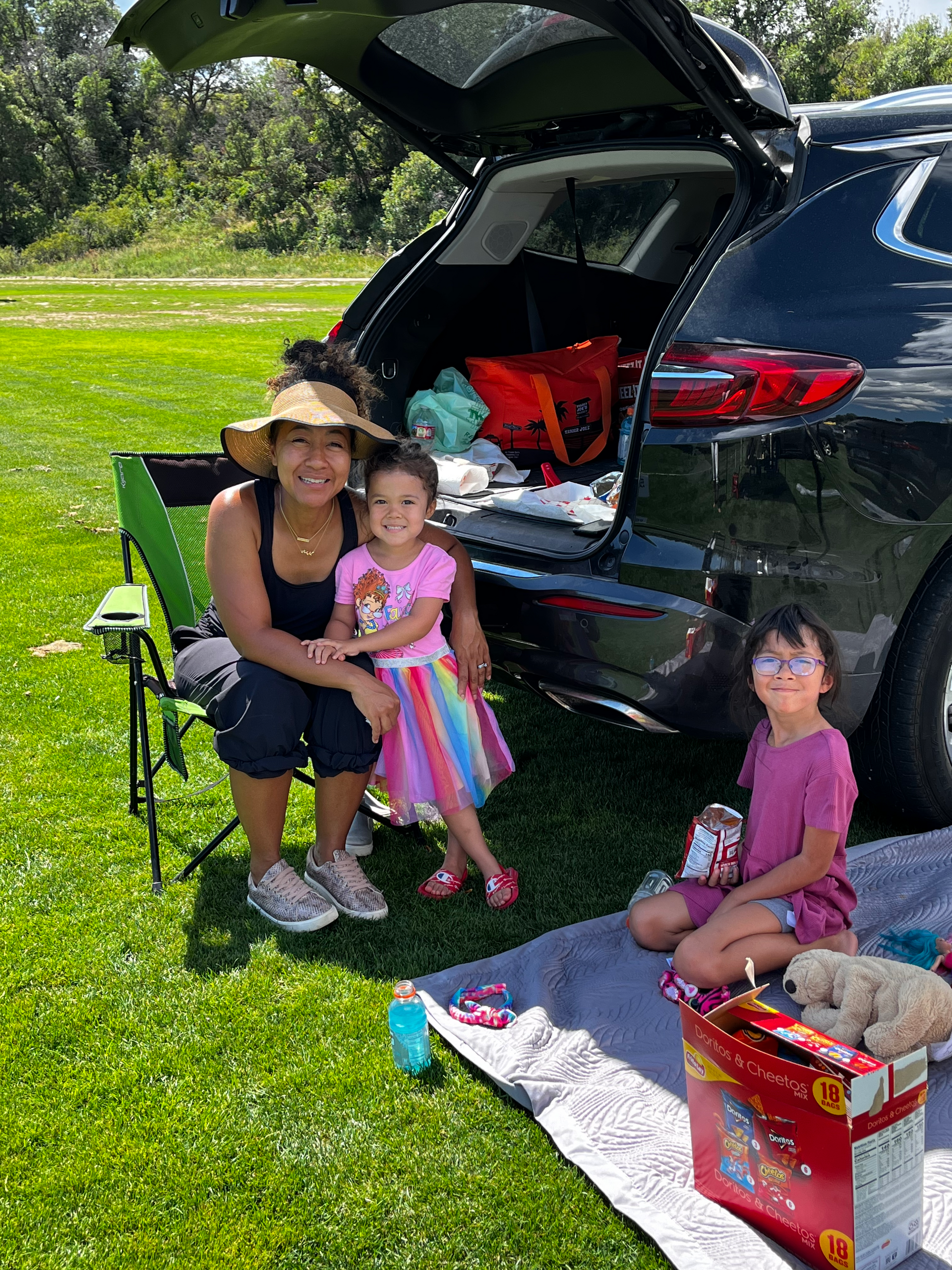 A woman and two little girls are sitting in the back of a car.