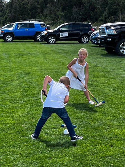 A boy and a girl are playing croquet on a lush green field.