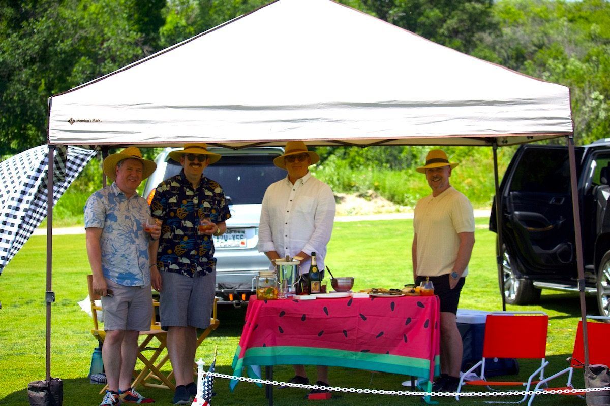 A group of men are standing under a tent with a watermelon tablecloth.