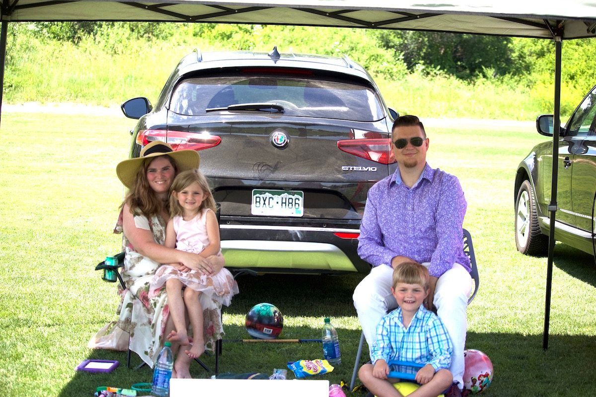 A family is sitting under a tent in front of a car.