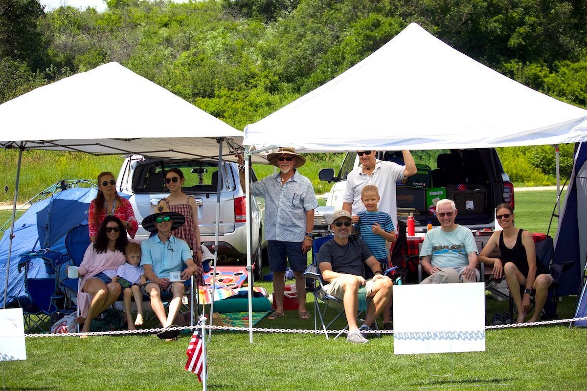 A group of people are sitting under tents in a field.