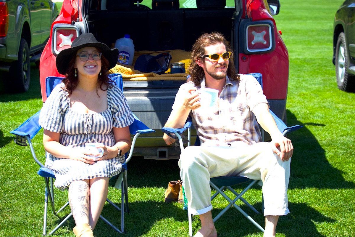 A man and a woman are sitting in chairs in front of a red jeep