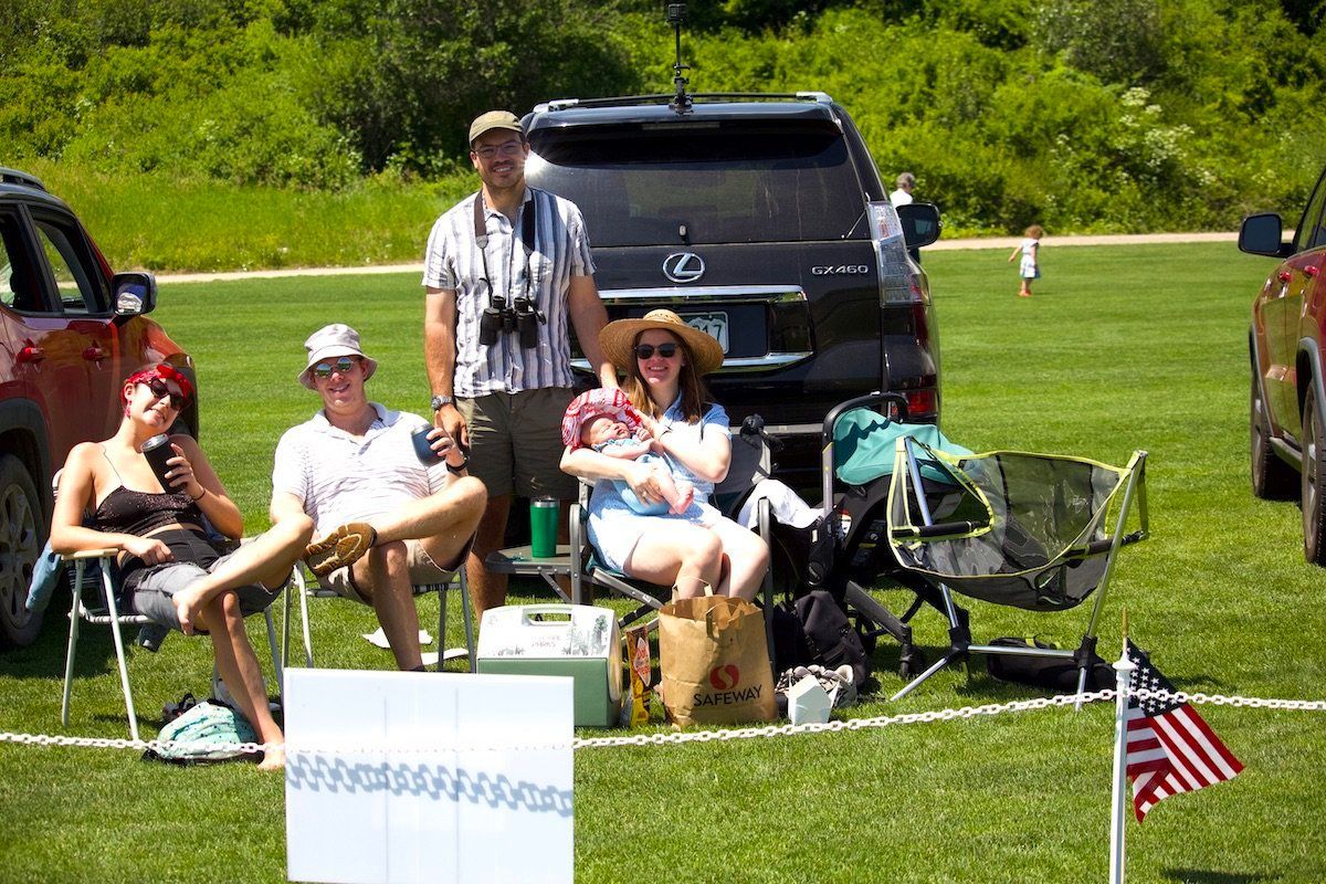 A group of people are sitting in chairs in front of a car.