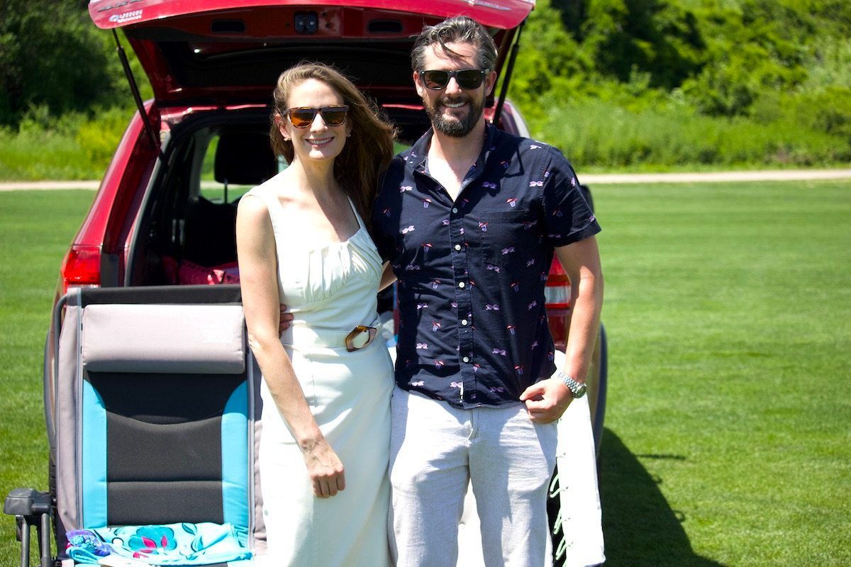 A man and a woman are posing for a picture in front of a red car.