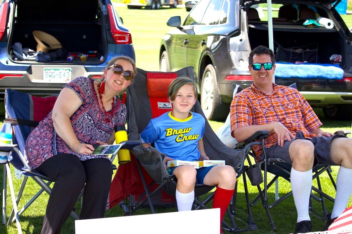 A family is sitting in chairs in front of a car.