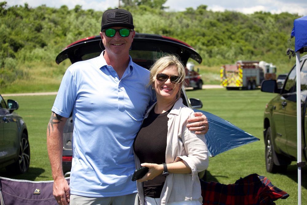 A man and a woman are posing for a picture in front of a car.