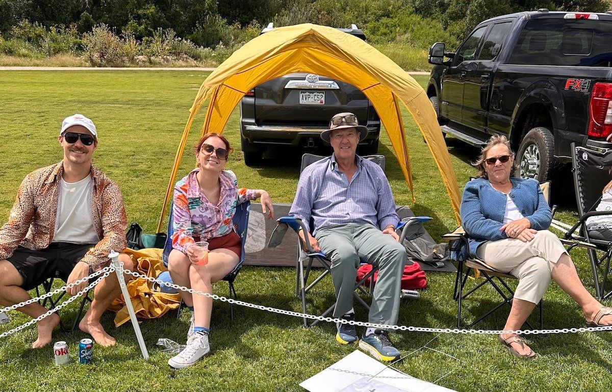 A group of people are sitting under a tent in a field.