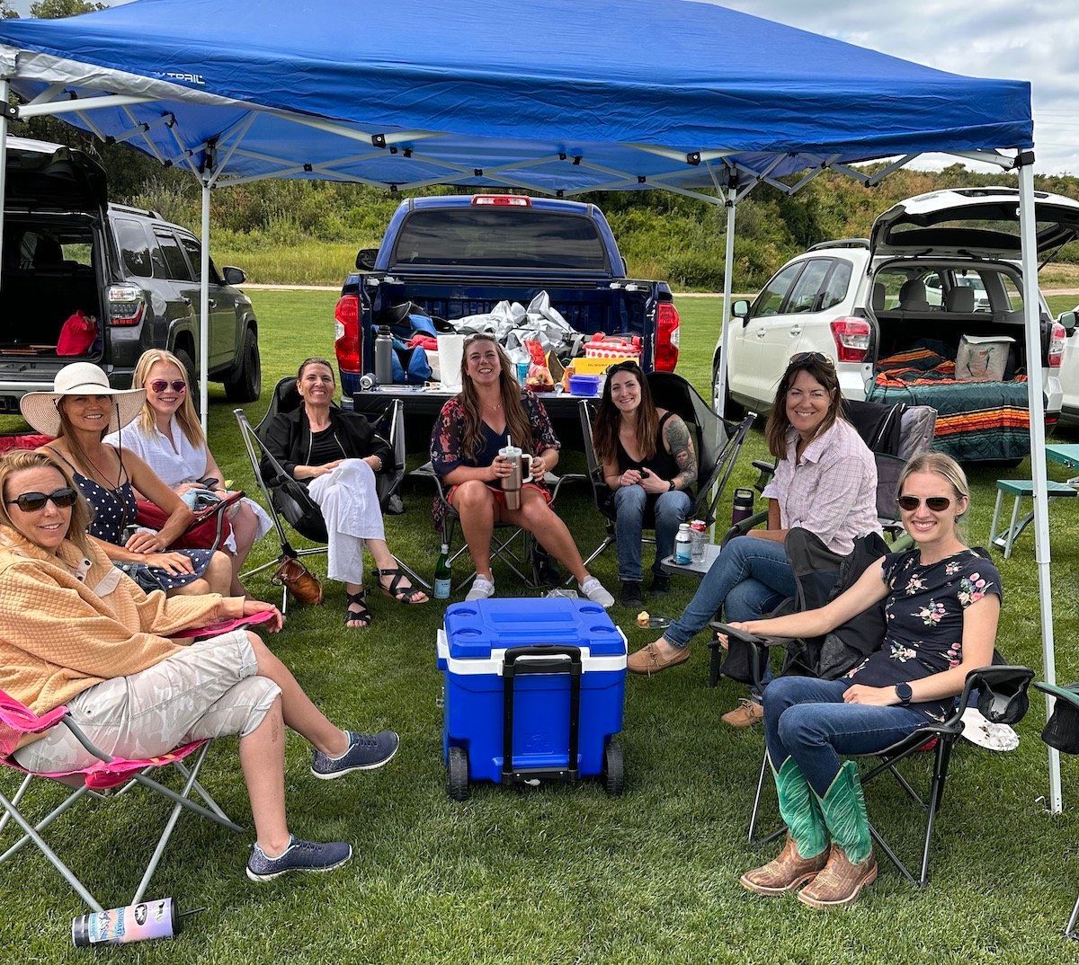 A group of people are sitting under a blue tent in a field.