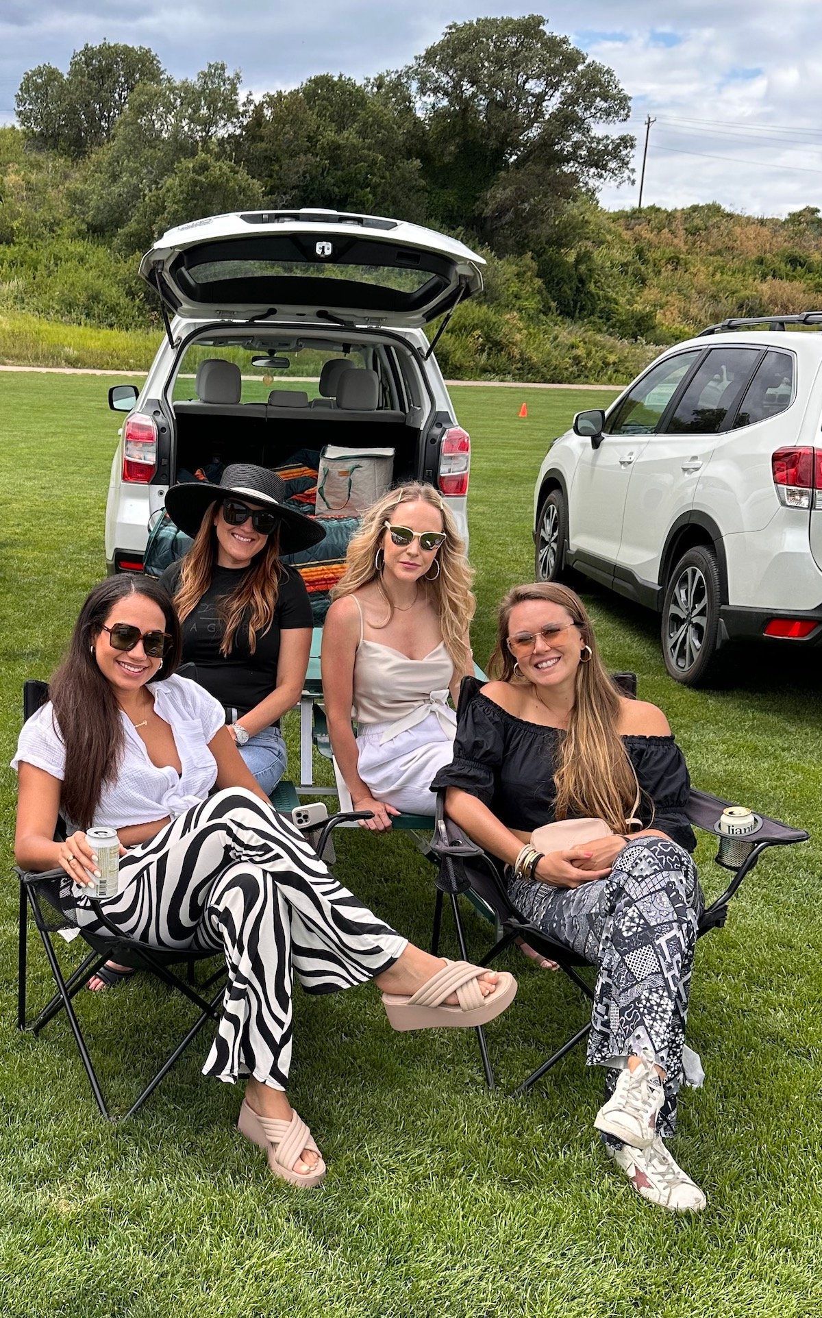 A group of women are sitting in chairs in front of a car.