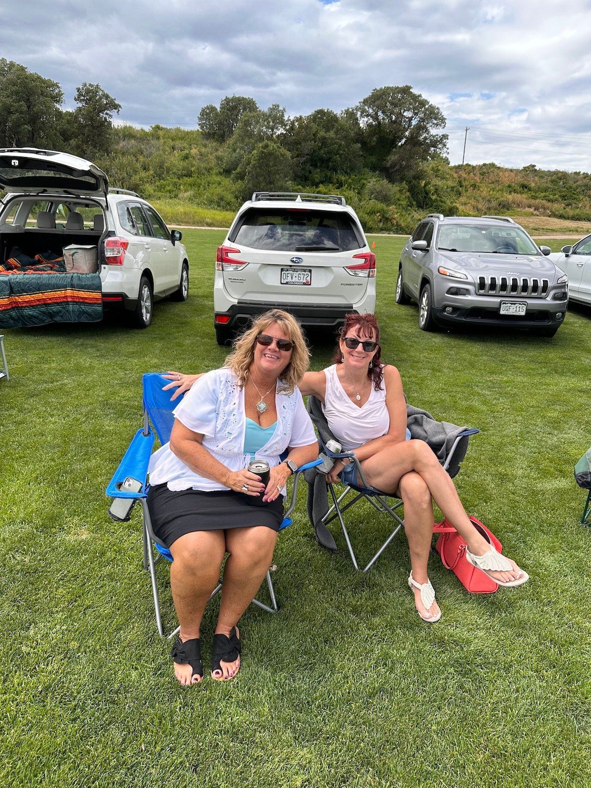 Two women are sitting in chairs in a grassy field.