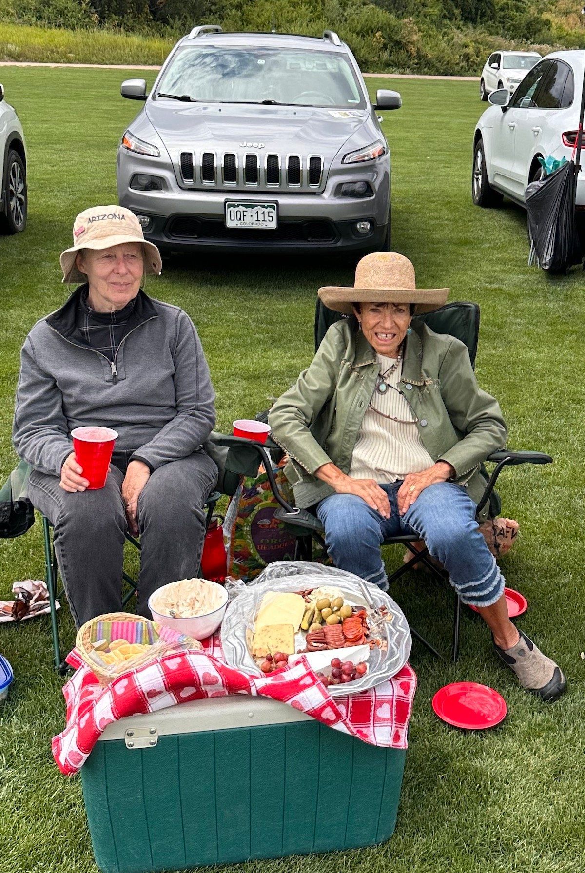 Two women are sitting in chairs in front of a picnic table.