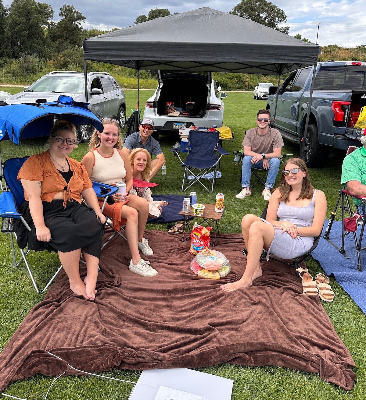 A group of people are sitting on a blanket in a field.