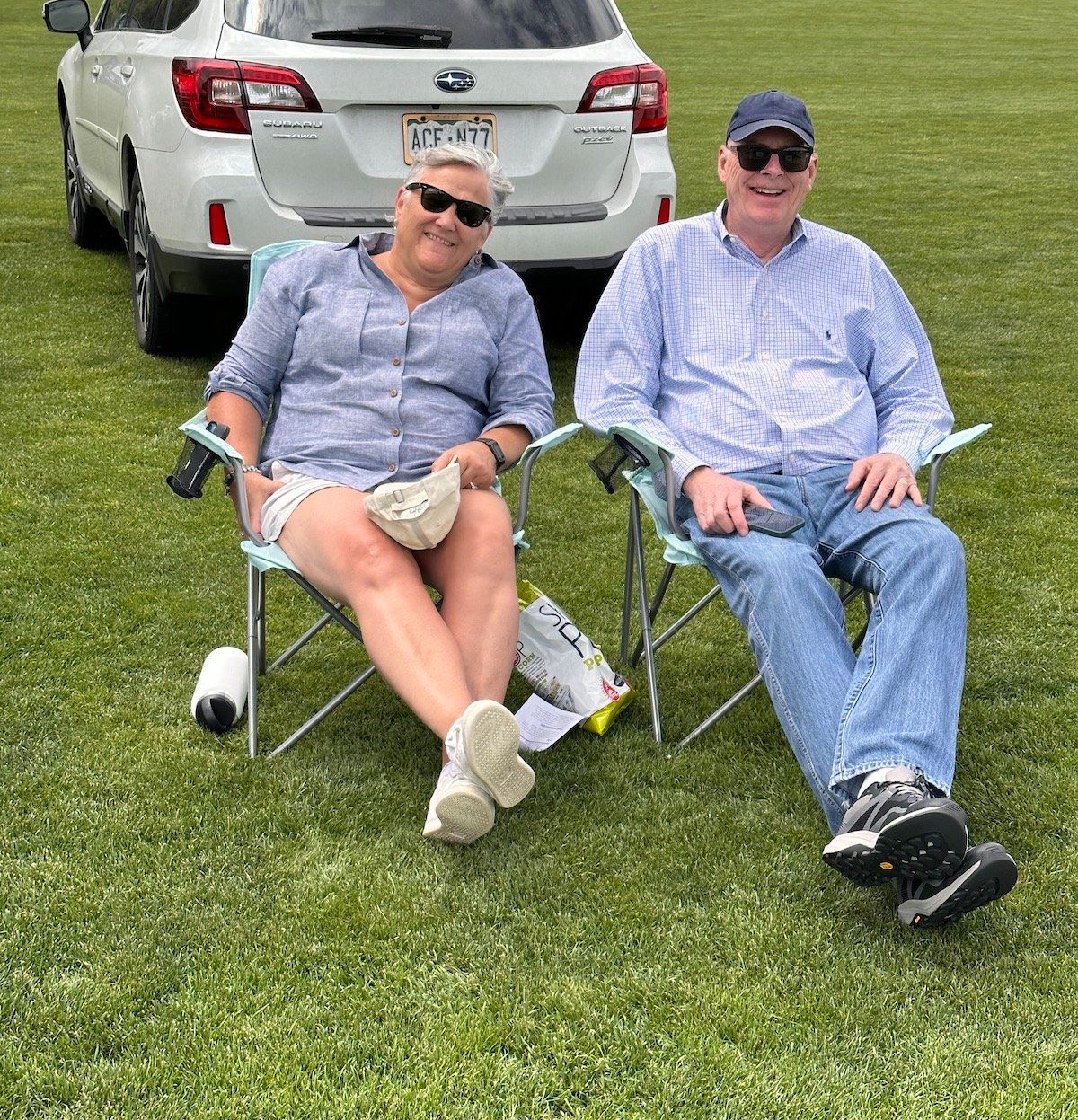 A man and a woman are sitting in folding chairs in the grass.