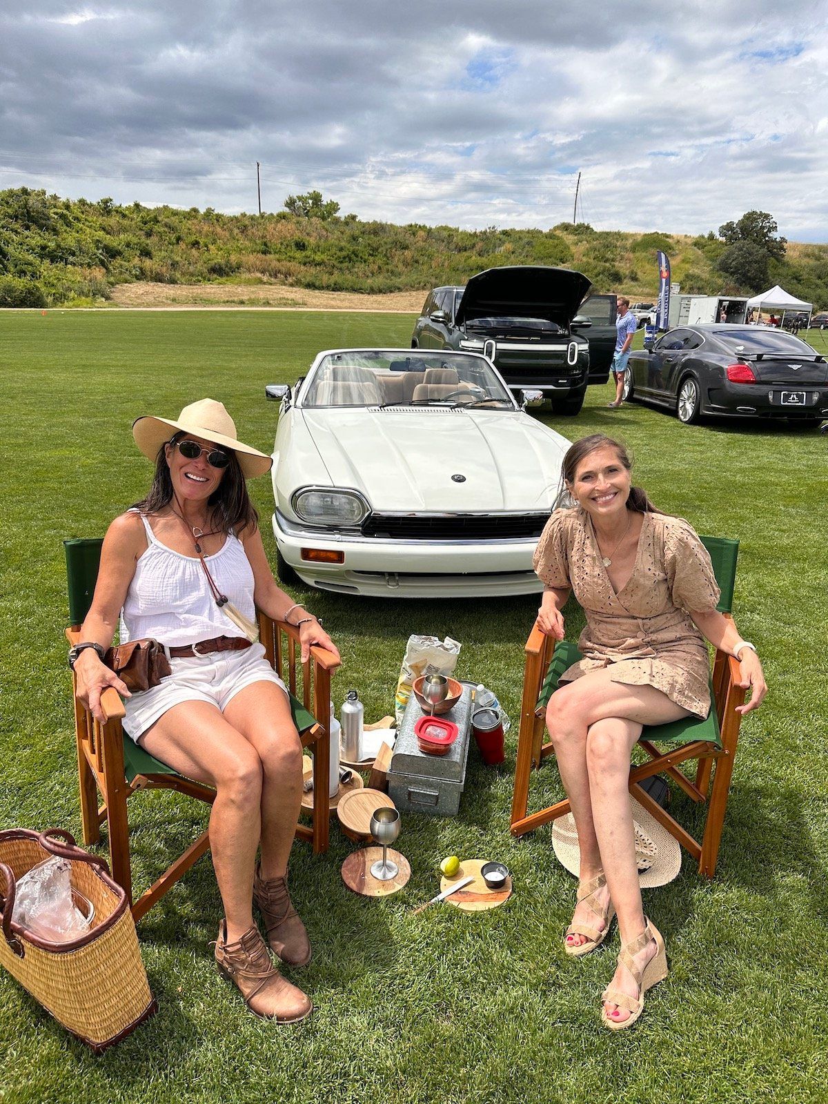 Two women are sitting in chairs in front of a white car.