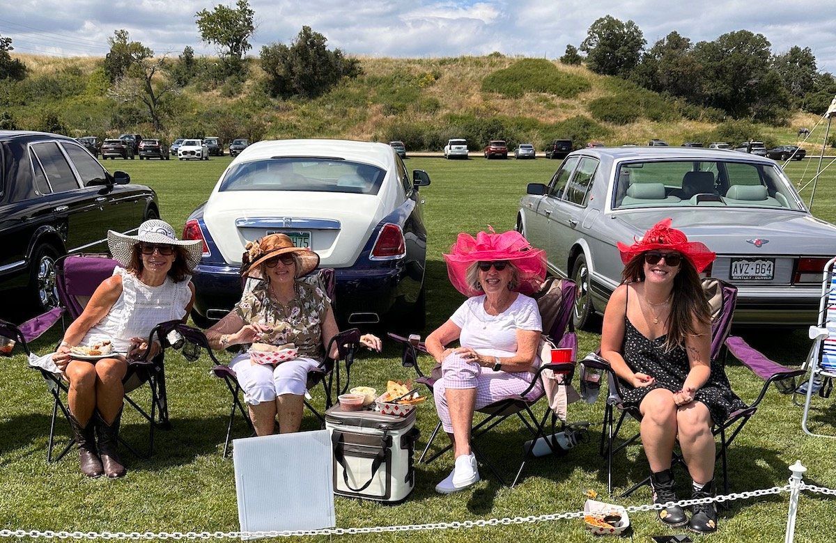 A group of women are sitting in chairs in front of cars at a car show.
