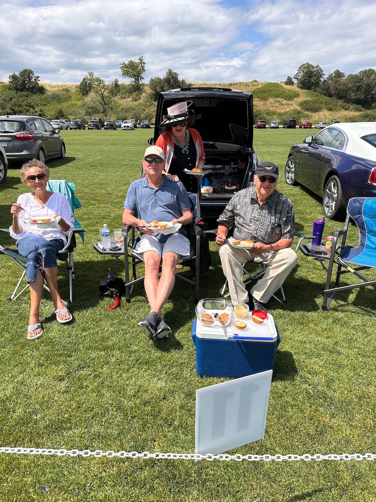 A group of people are sitting in chairs in a field eating food.
