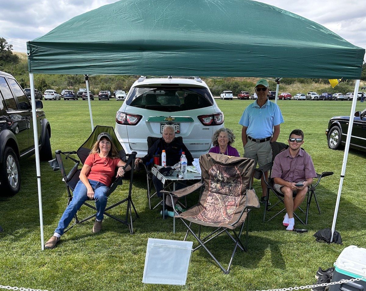 A group of people are sitting under a tent in a field.
