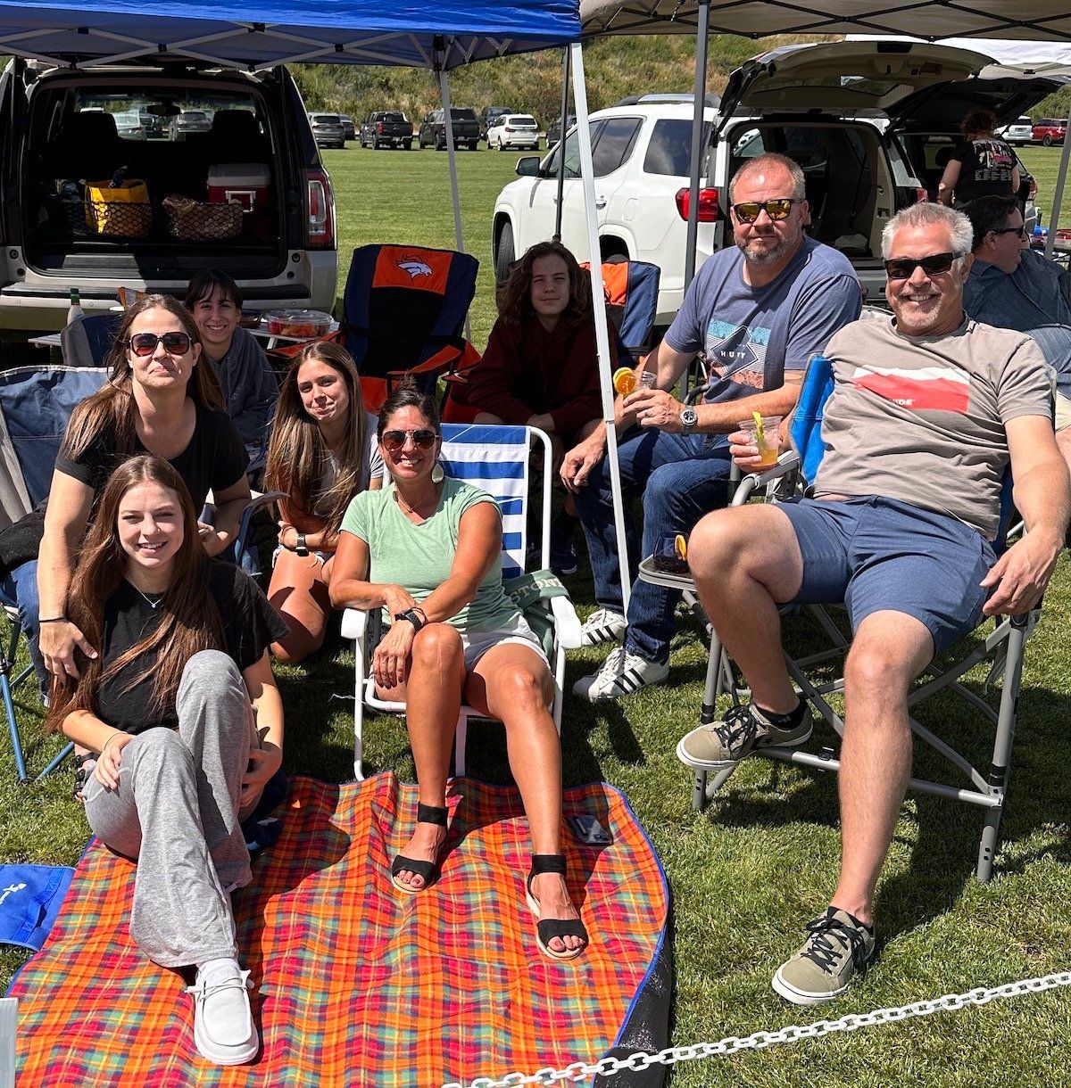 A group of people are sitting on a blanket under a tent in a field.